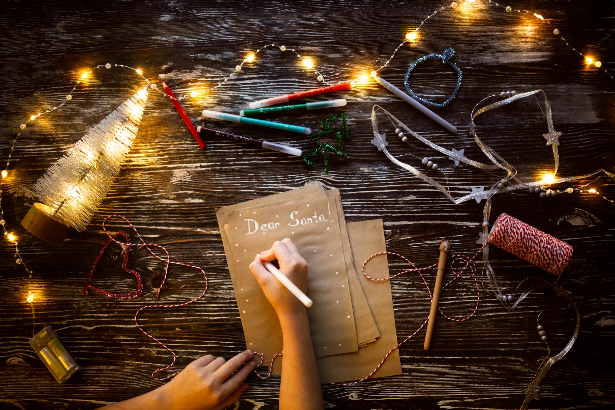 Children's hands write Dear Santa, Child writes a Letter to Santa Claus on craft paper, top view